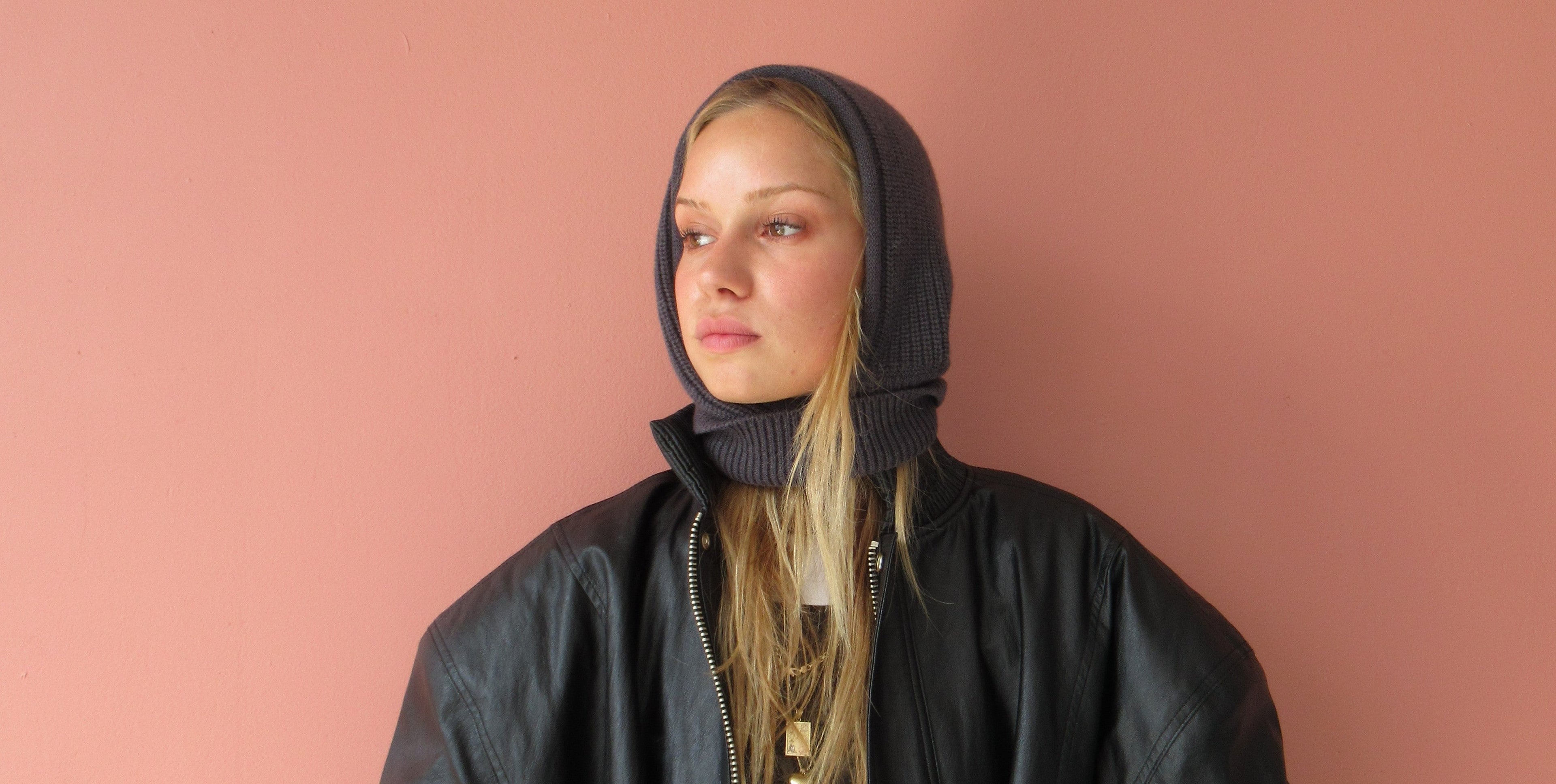 Person wearing a black jacket and hood against a pink background